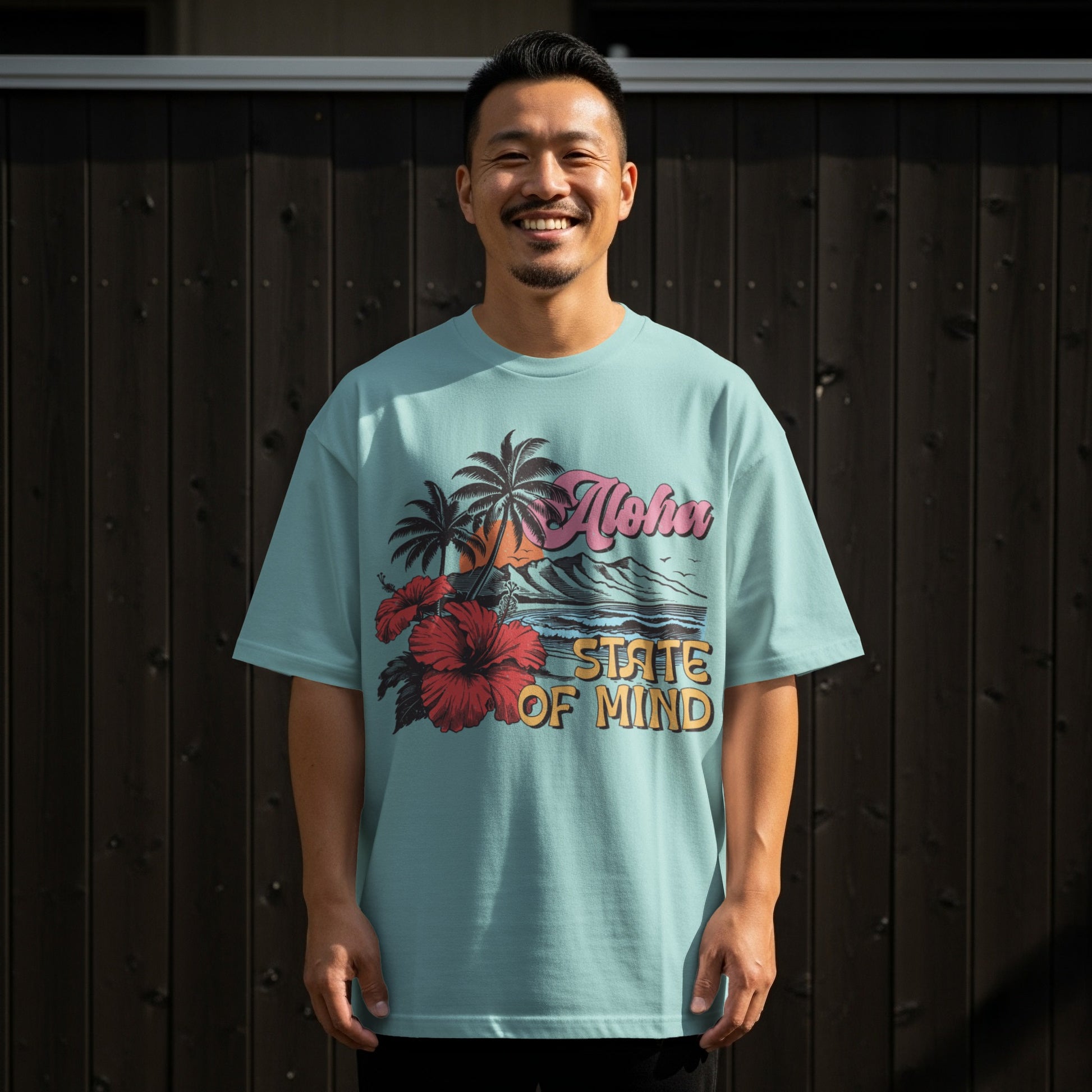 Man wearing light blue t-shirt with Aloha State of Mind palm trees and hibiscus graphic.