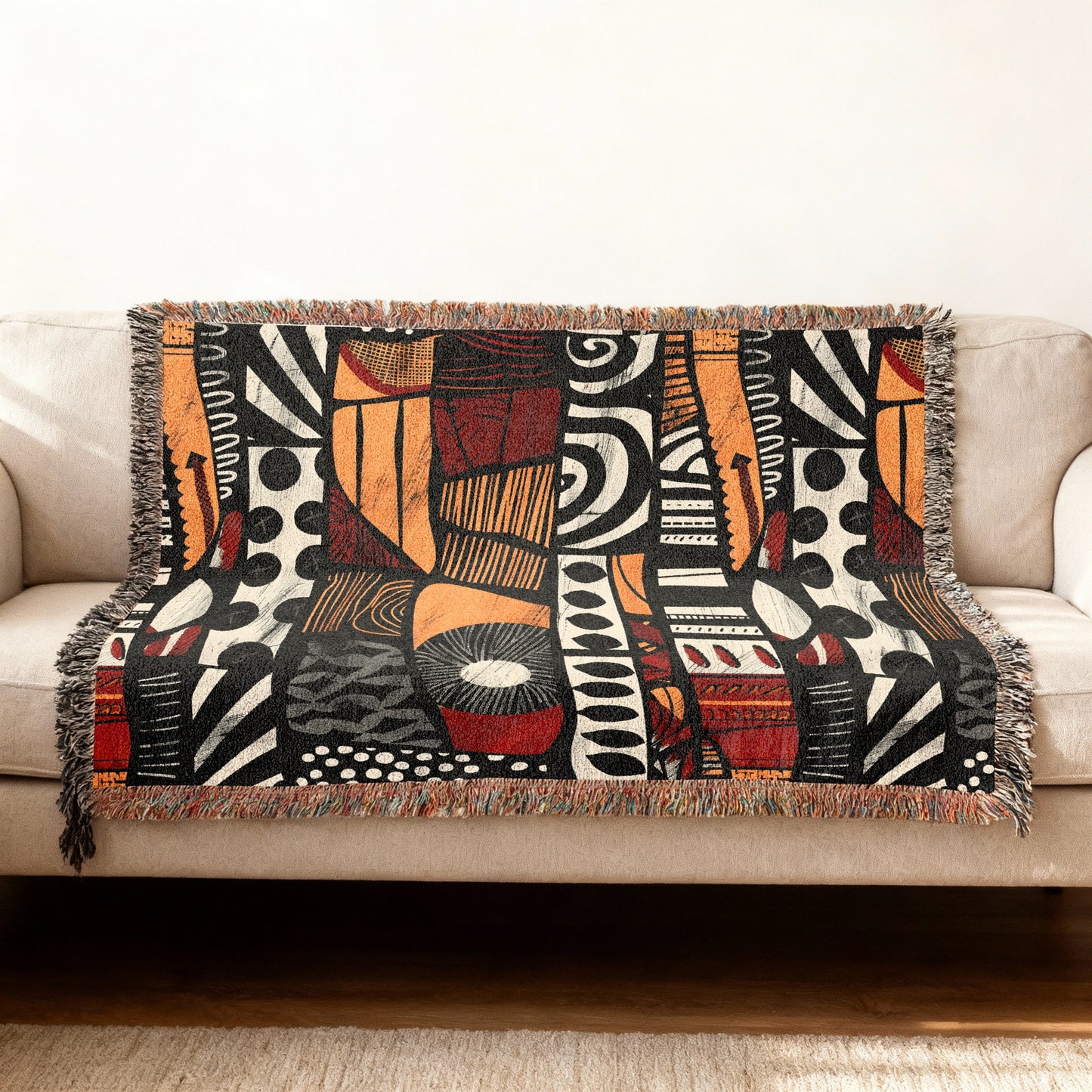 Woven blanket with abstract black, orange, and red geometric pattern draped over a sofa.