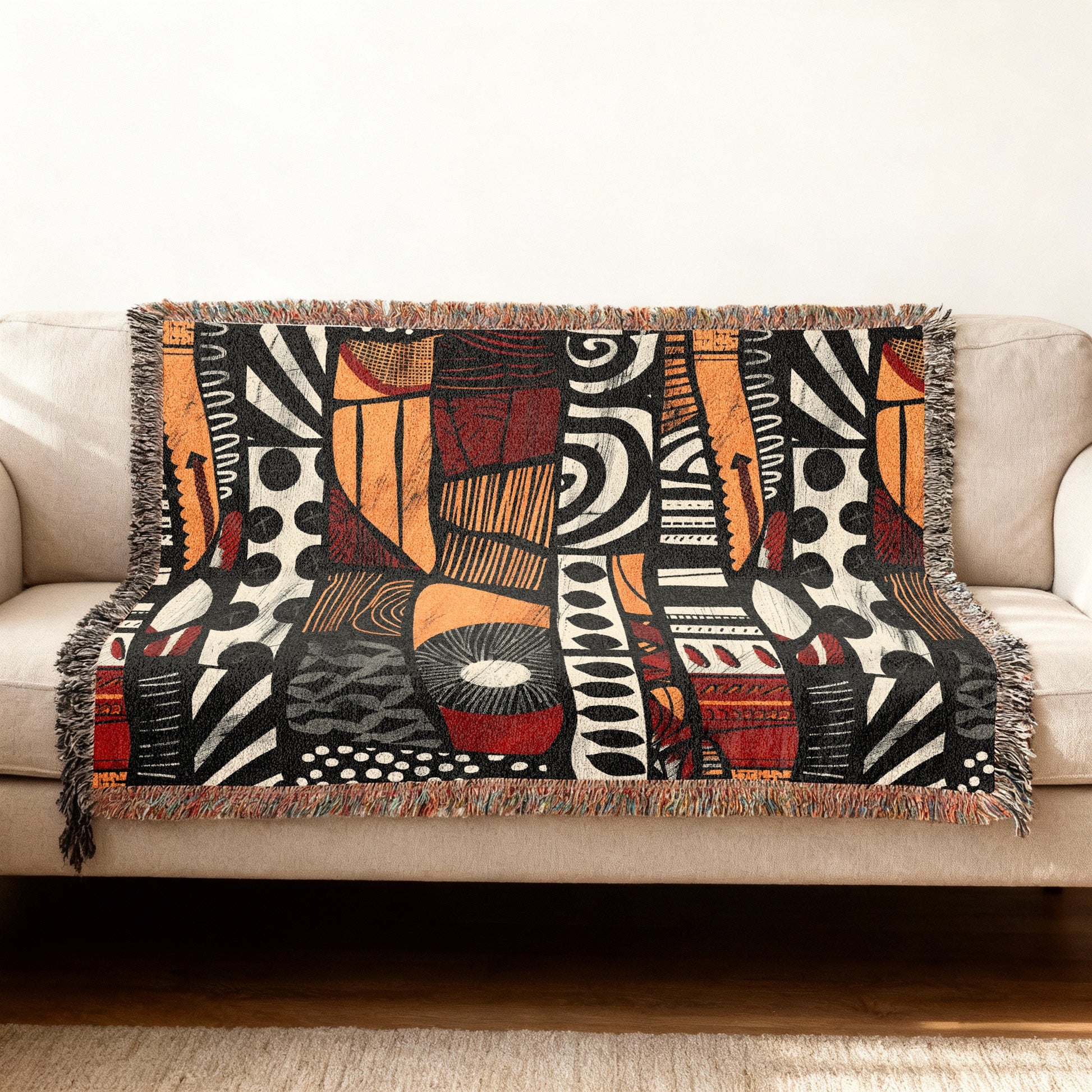Woven blanket with abstract black, orange, and red geometric pattern draped over a sofa.