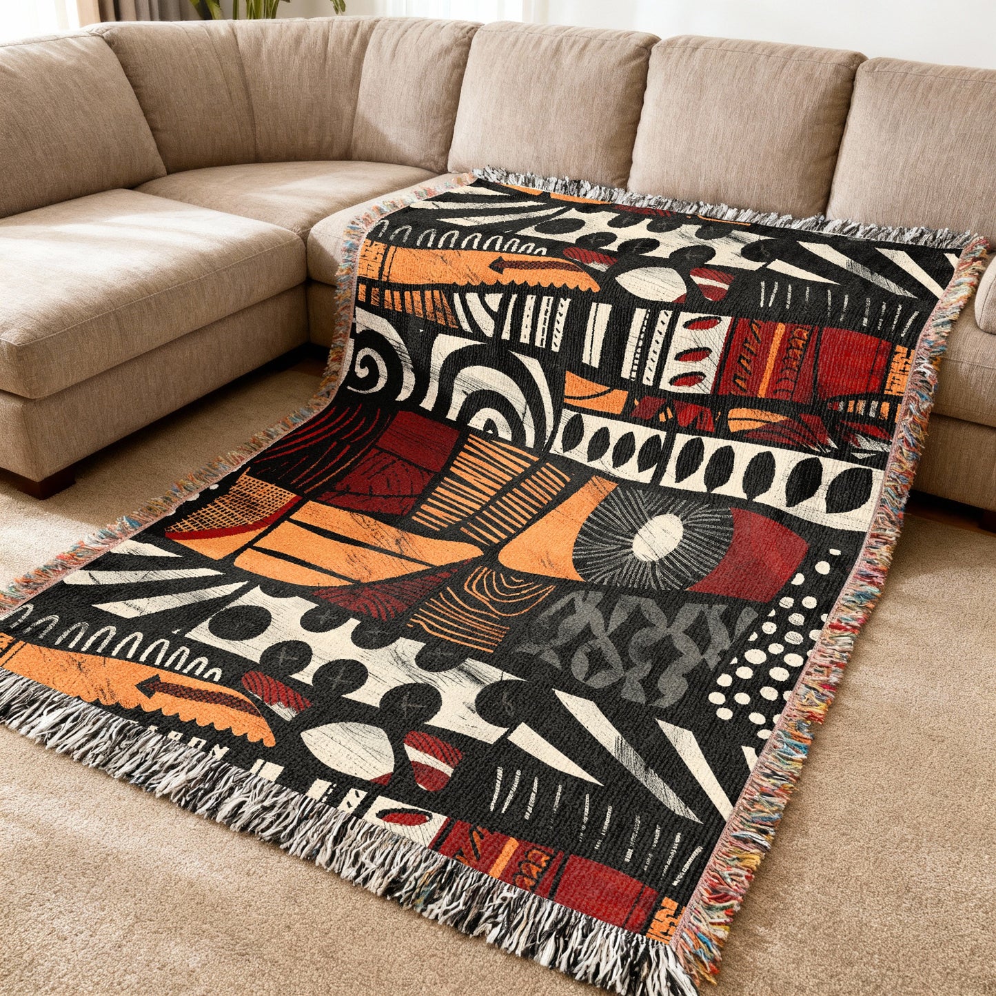 Fringed throw blanket with a black, orange, and red abstract woven pattern.