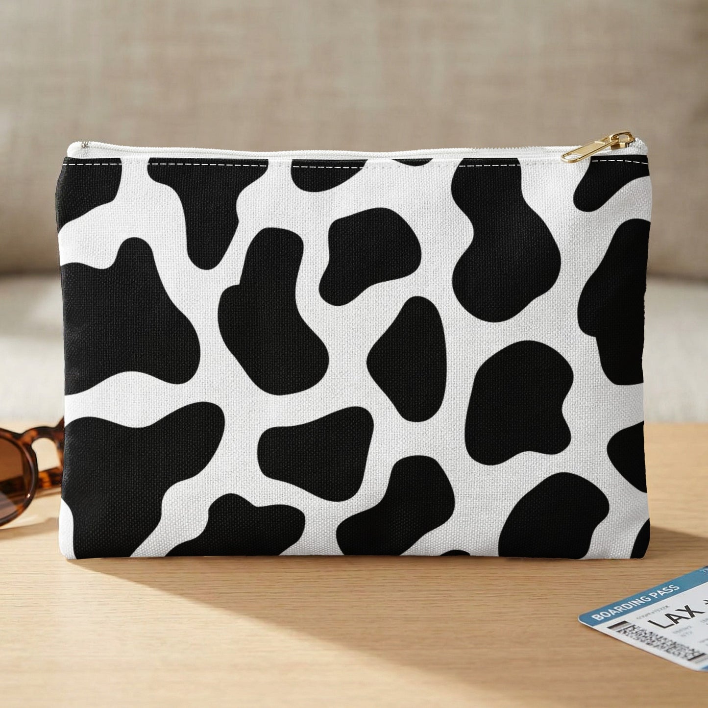 Black and white cow print cosmetic bag with gold zipper on a desk.