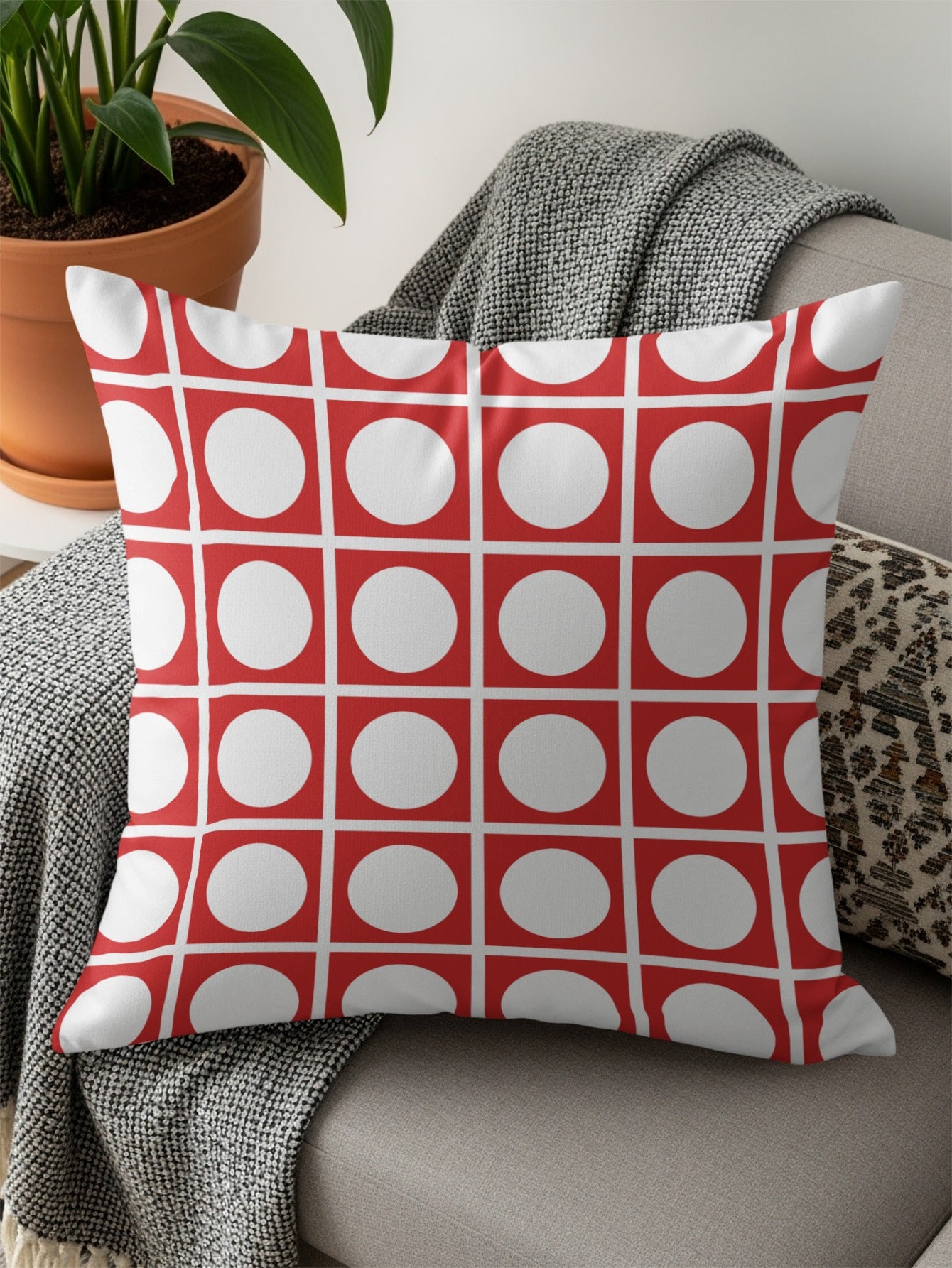 Red and white polka dot pillow on a grey couch with a throw blanket.