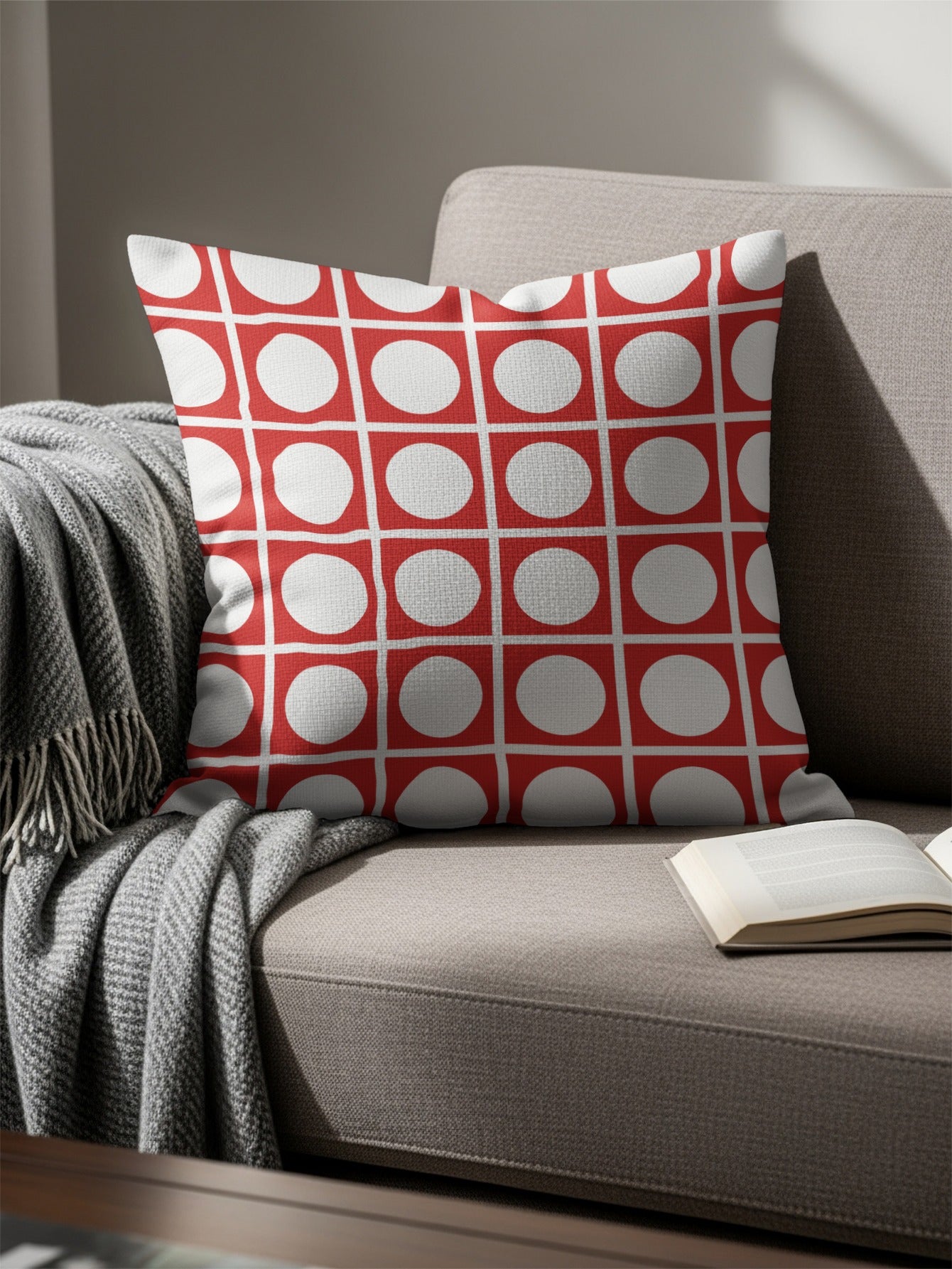 Red and white geometric circle pattern pillow on a sofa with a blanket and book.