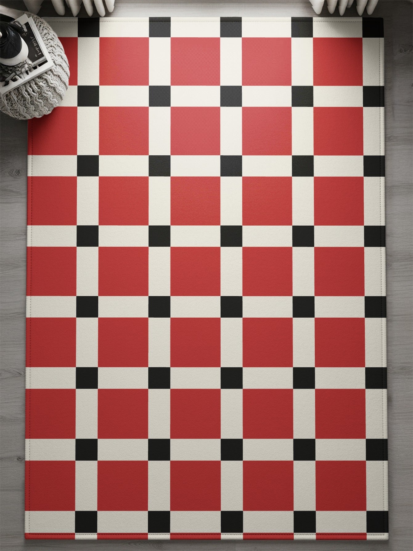 Red, white, and black checkered rug with stitched edges on wooden floor.