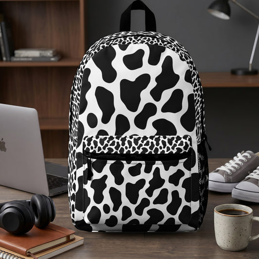 Black and white cow print backpack with front pocket and mesh side pockets.