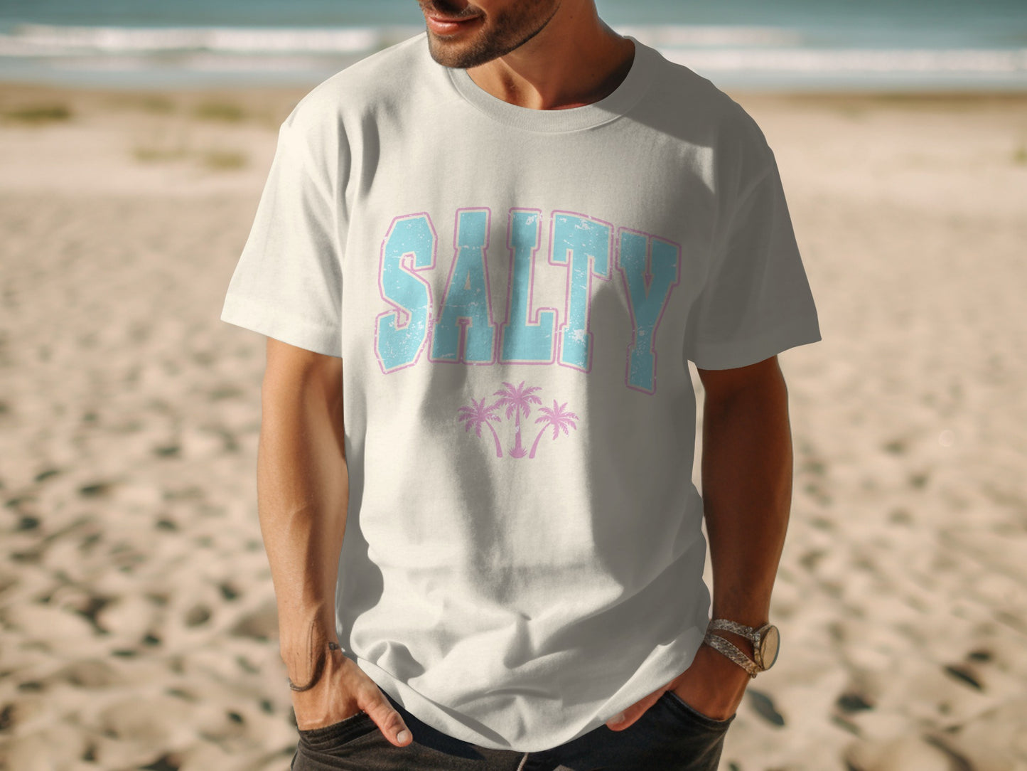 White t-shirt with "SALTY" text and pink palm trees on a beach.
