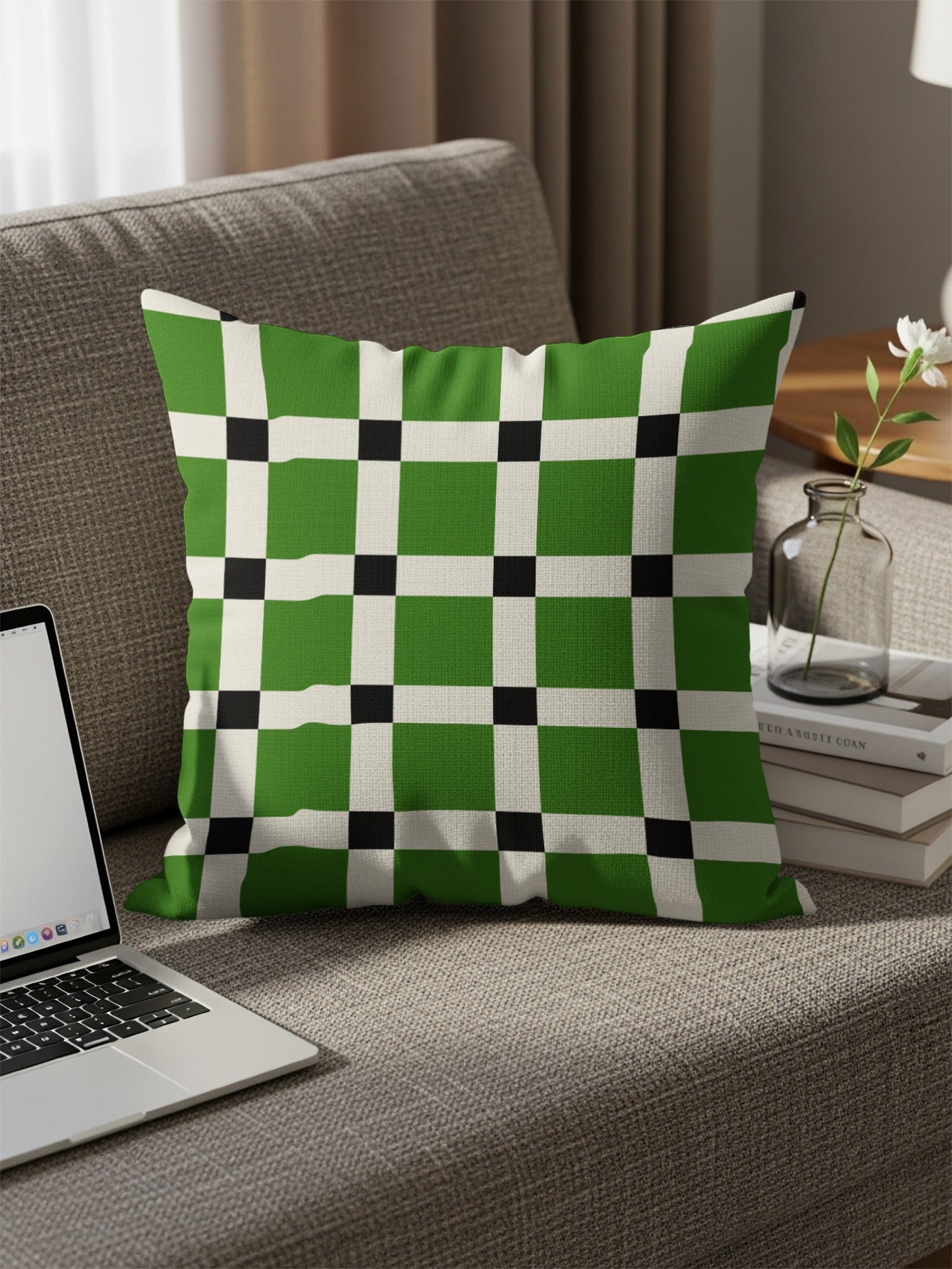 Green, white, and black checkered throw pillow on a sofa with a laptop and books.