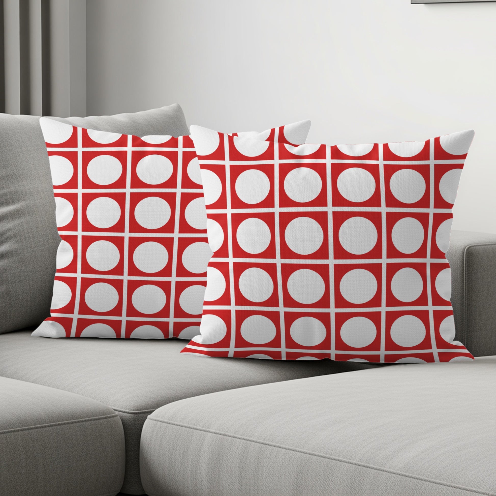 Two red and white geometric pattern throw pillows on a gray sectional sofa.