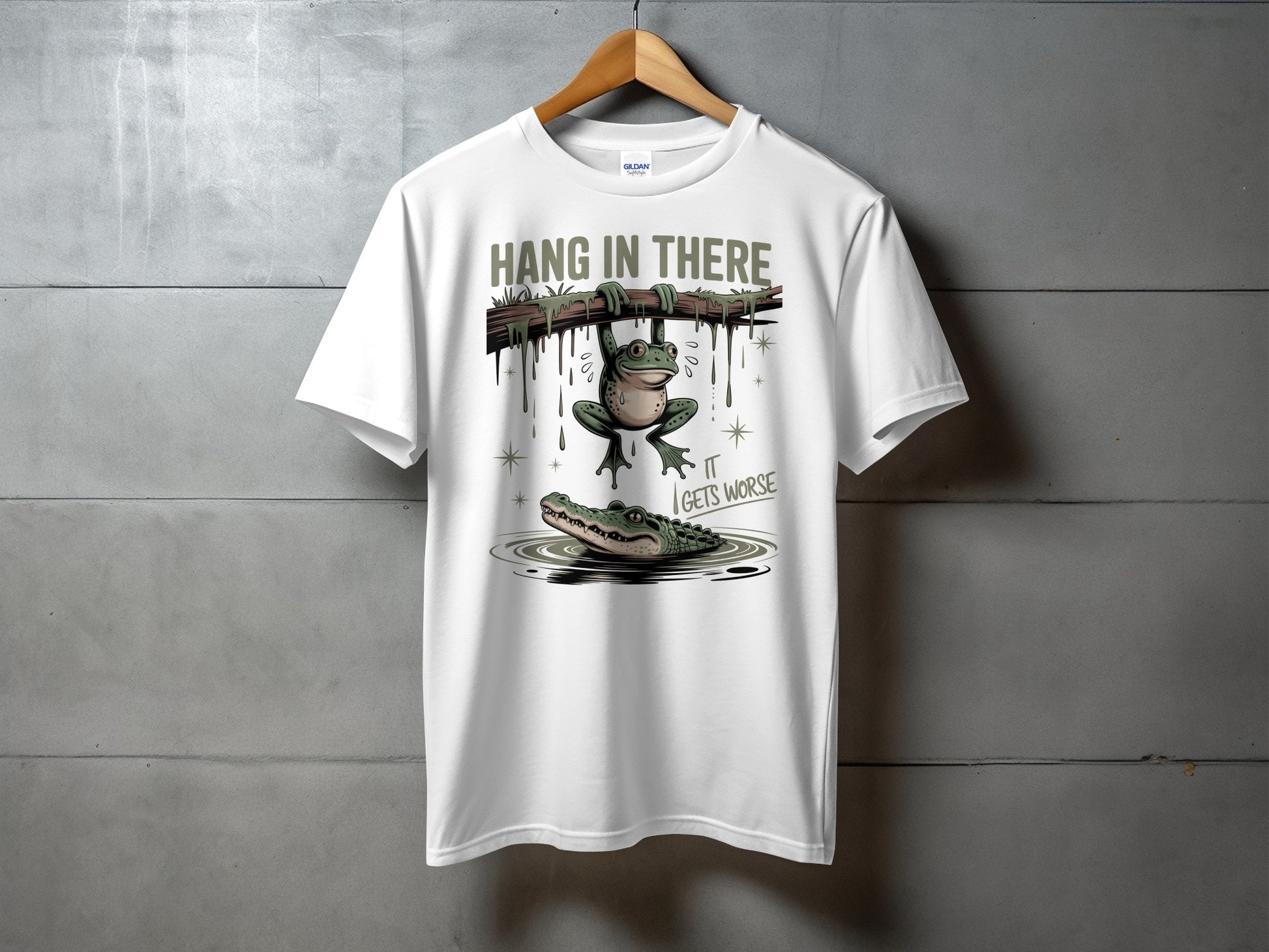 White t-shirt with frog hanging from branch above alligator in water.