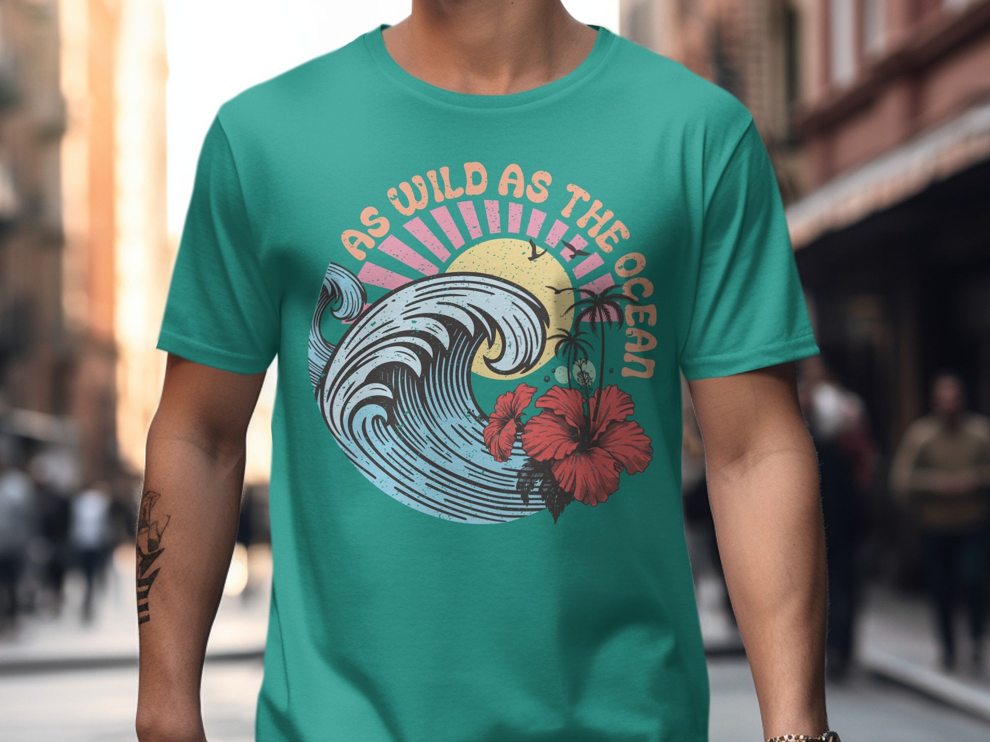 Teal t-shirt with "As Wild As The Ocean" text, a wave, and hibiscus flowers.