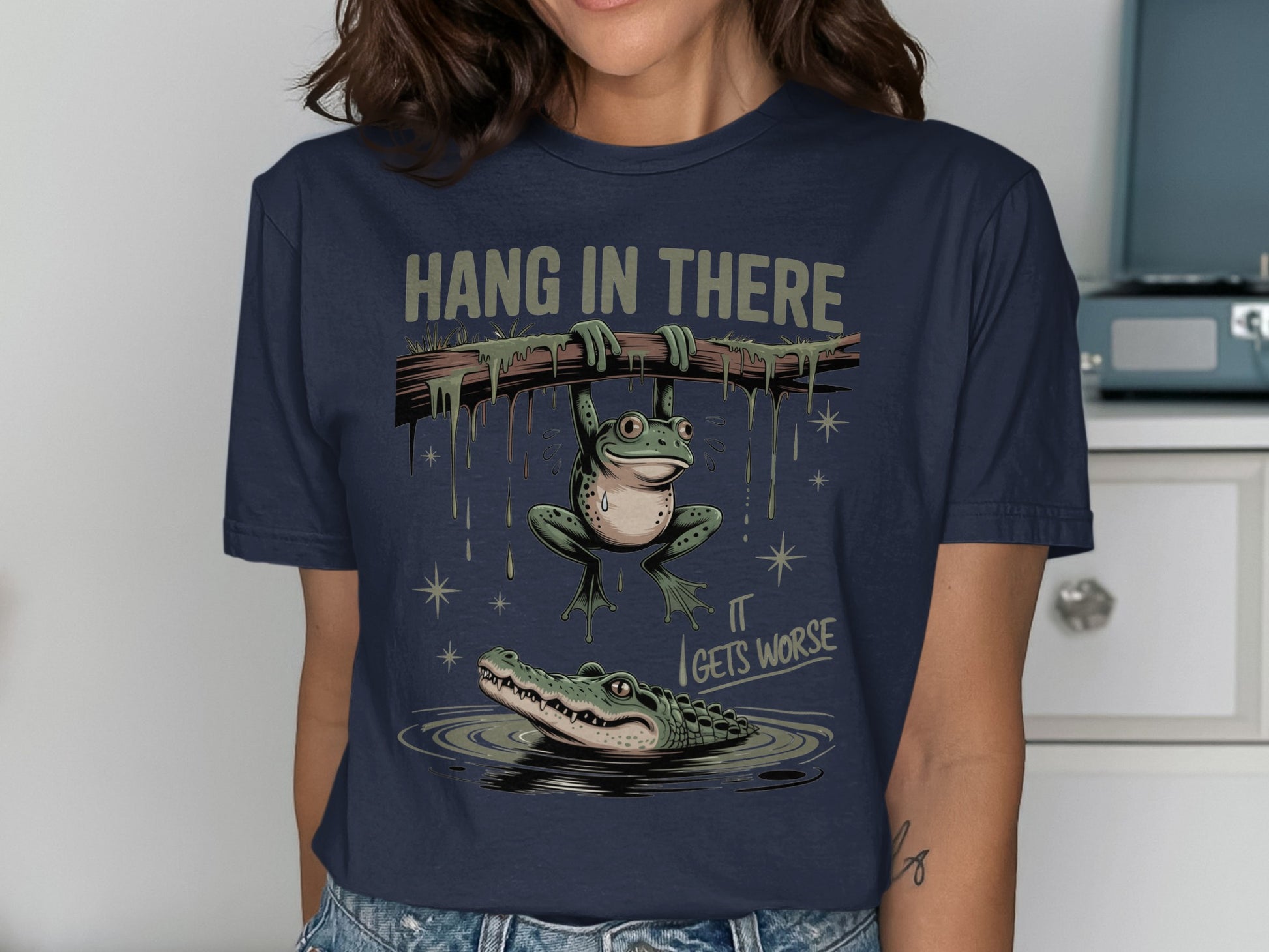 Frog hangs from branch over alligator, text "Hang in There It Gets Worse."