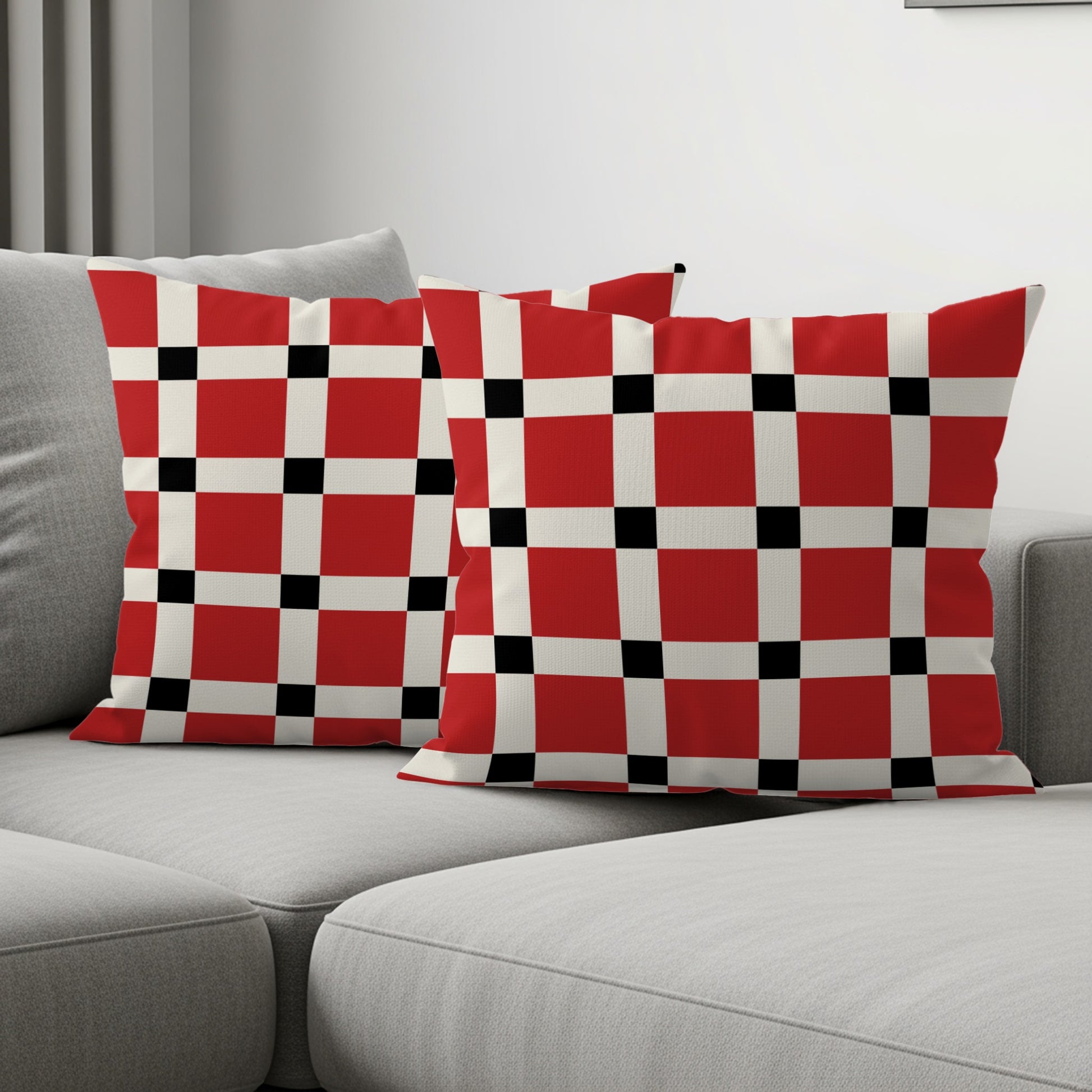 Two throw pillows with a red, white, and black checkered pattern on a gray couch.
