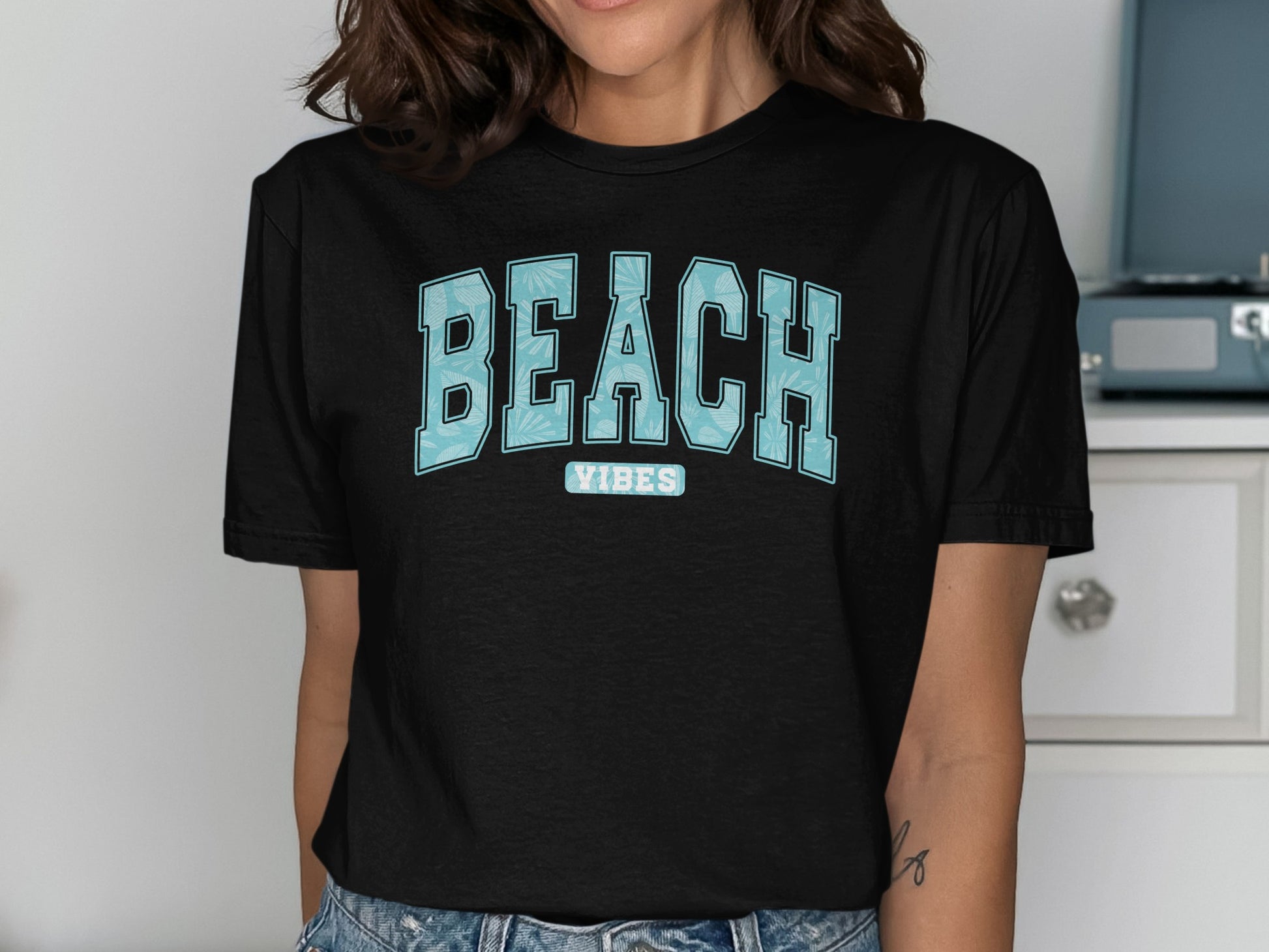 Black t-shirt with "BEACH VIBES" in blue tropical print lettering.