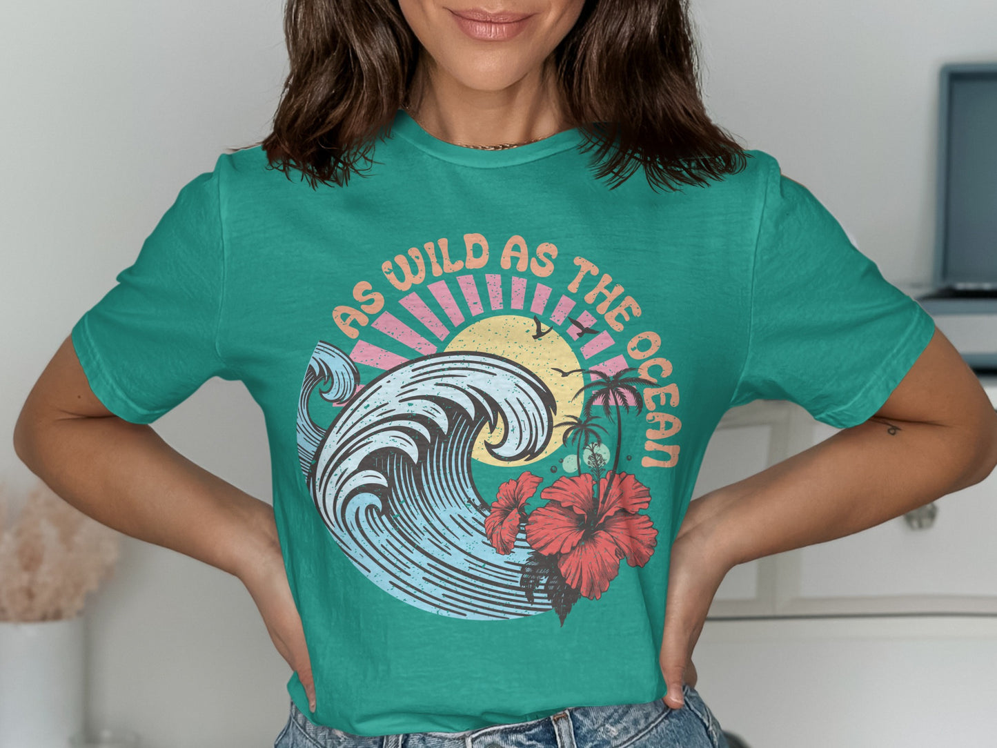 Teal t-shirt with "As Wild As The Ocean" text and a graphic of a wave, sun, and flowers.