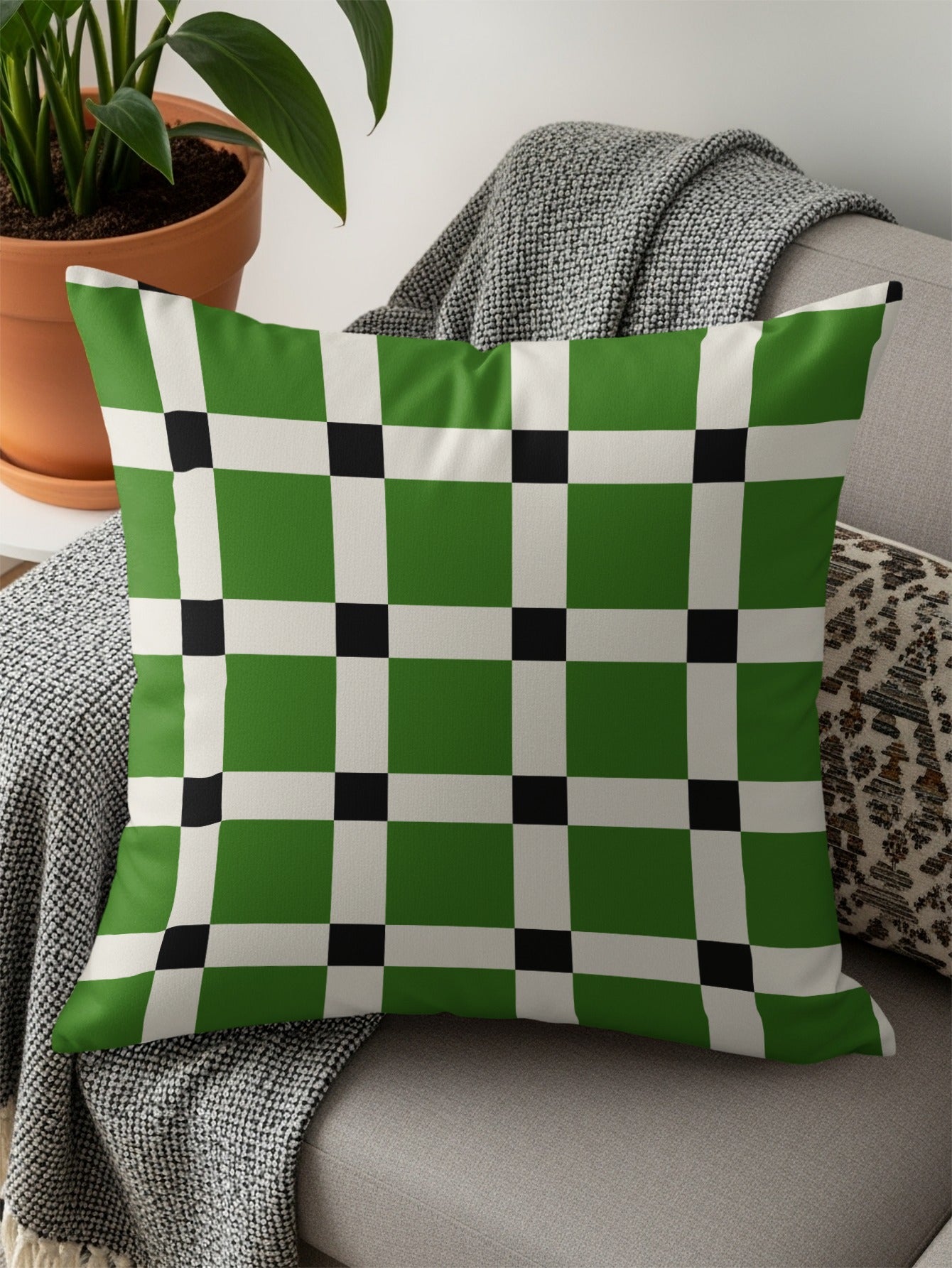 Green, white, and black plaid throw pillow on a sofa with a blanket.