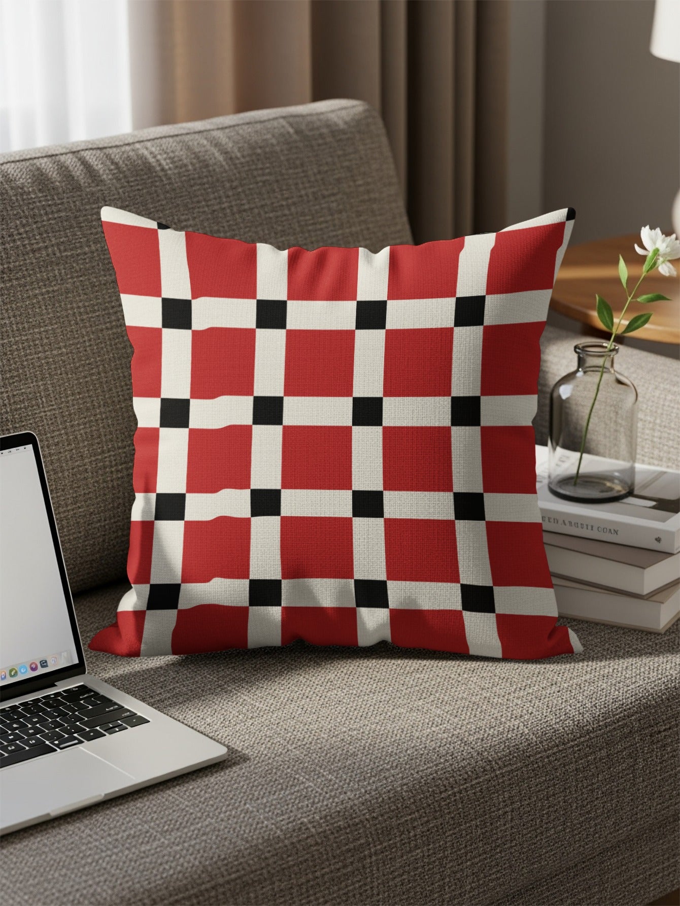 Red, white, and black checkered pillow on a gray couch with a laptop and books.