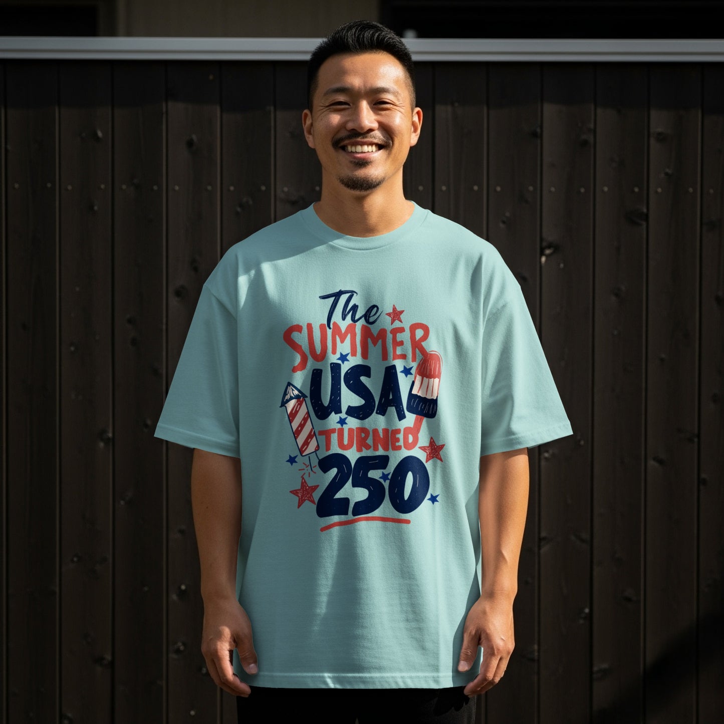 Man wearing a light blue t-shirt with "The Summer USA Turned 250" graphic.