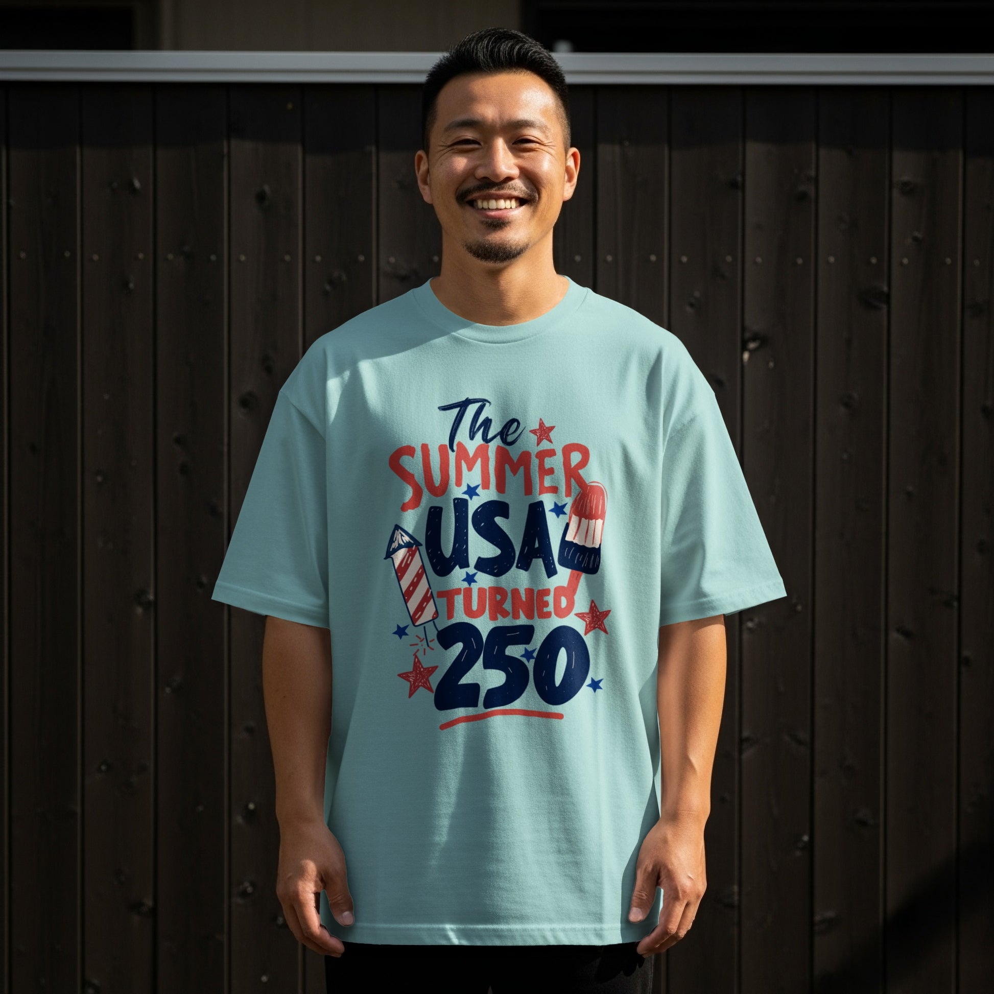 Man wearing a light blue t-shirt with "The Summer USA Turned 250" graphic.