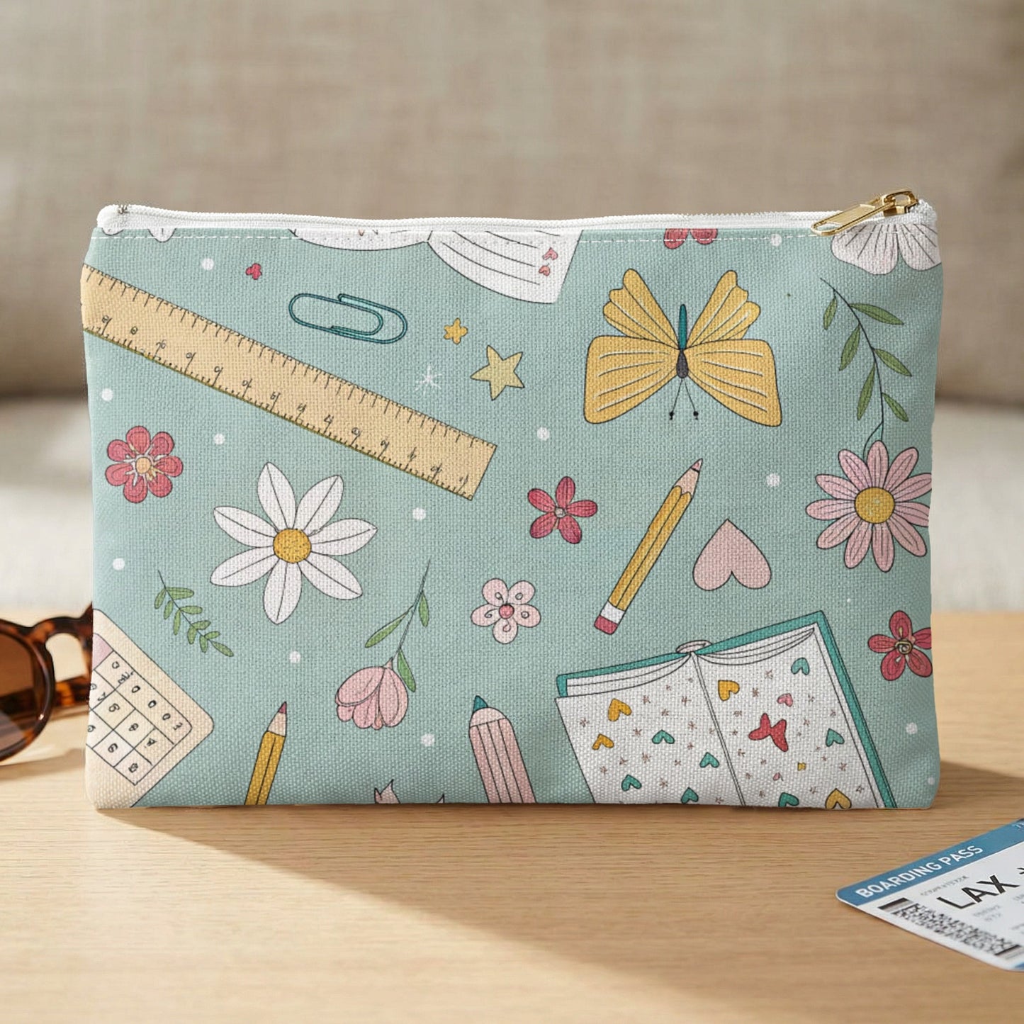 Teal pouch adorned with a ruler, butterflies, flowers, pencils, and an open book.