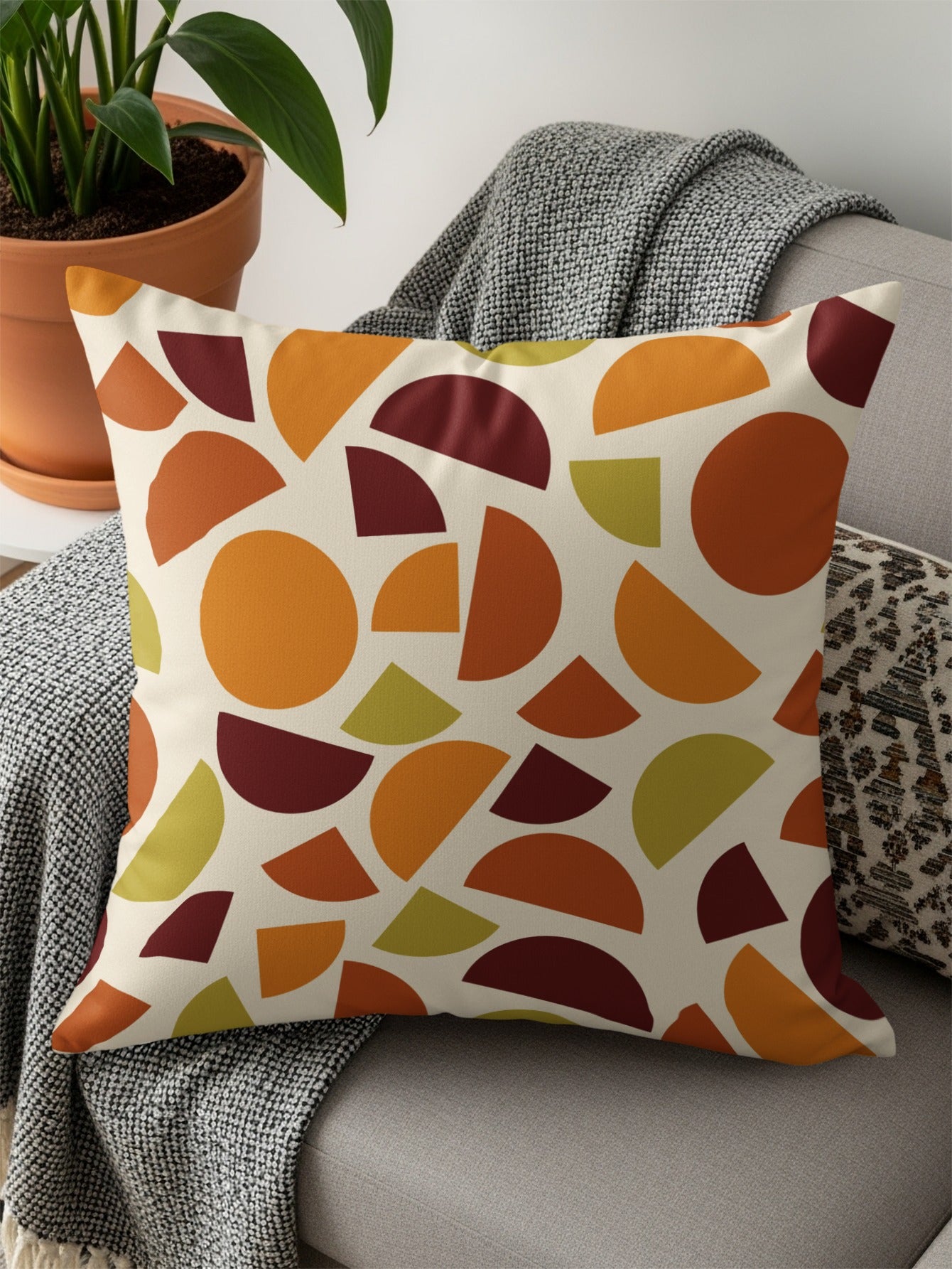 Cream pillow with scattered geometric shapes in orange, burgundy, and green.