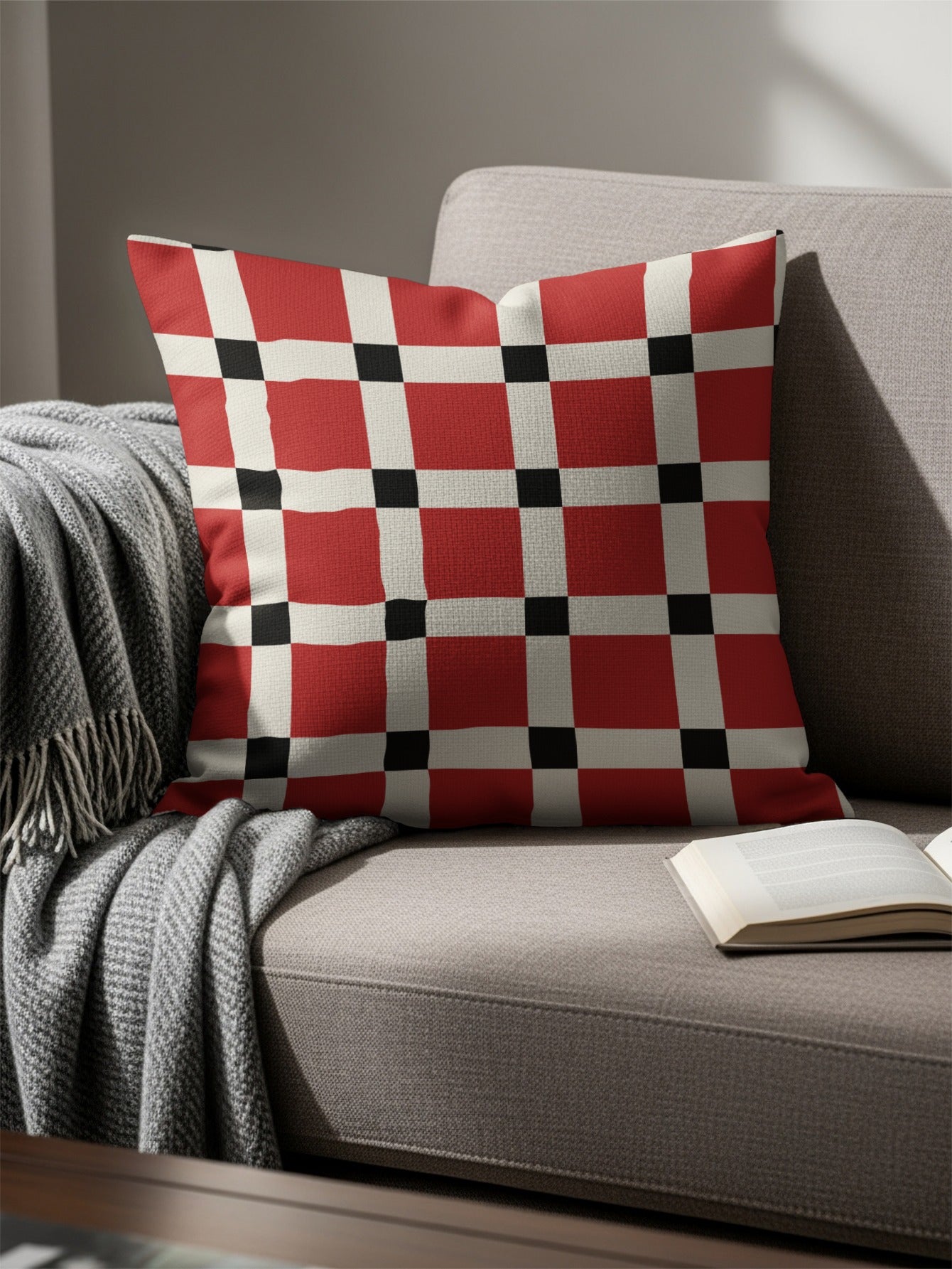 Square throw pillow with red, white, and black geometric pattern on a gray couch.