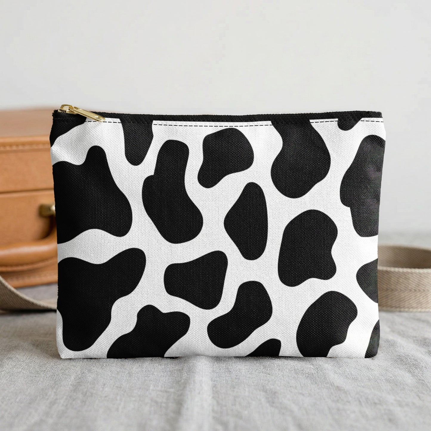 Small pouch with black and white cow print and gold zipper, set on gray fabric.