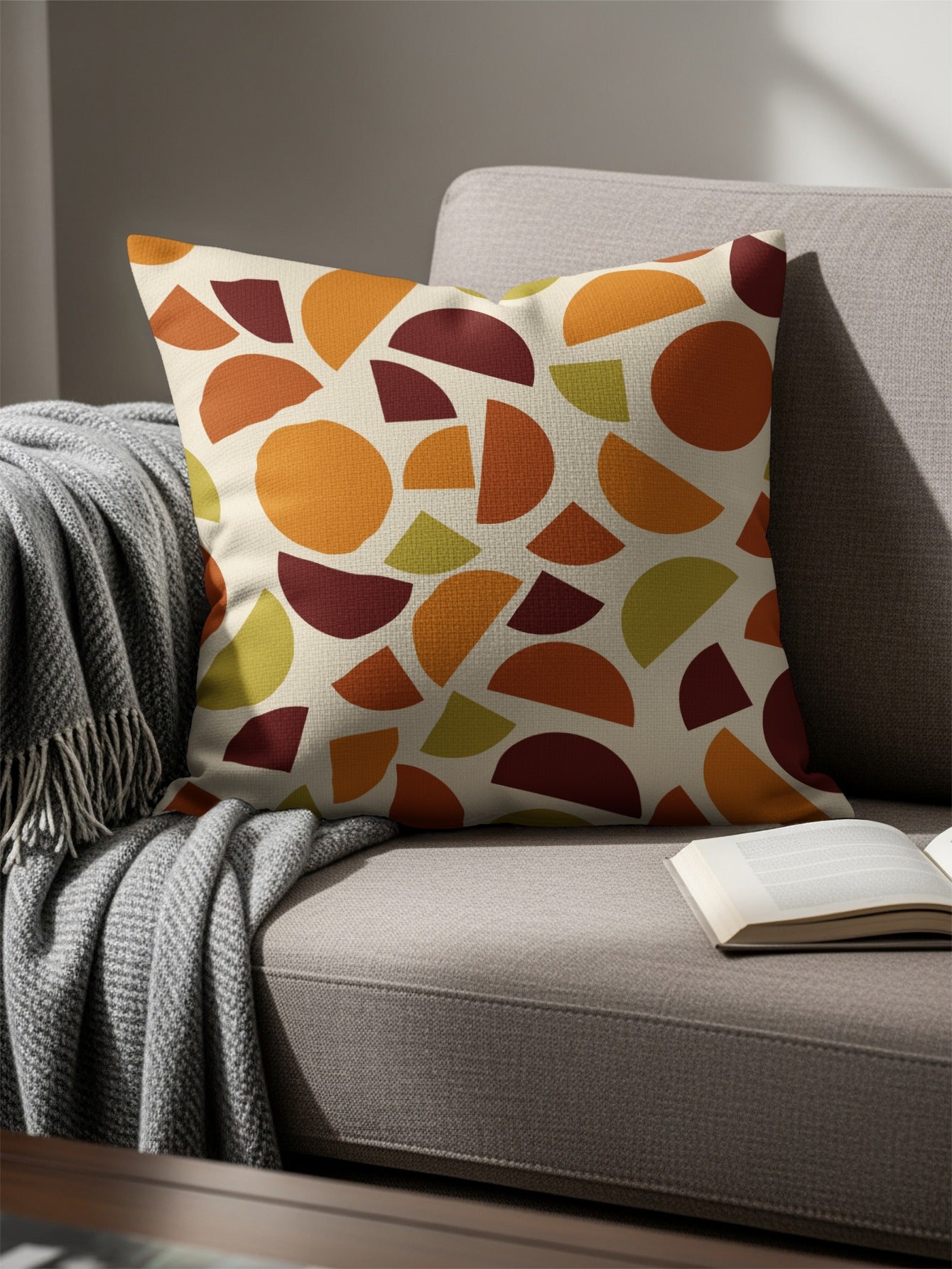 Pillow with abstract geometric pattern in warm tones on a sofa with throw and book.