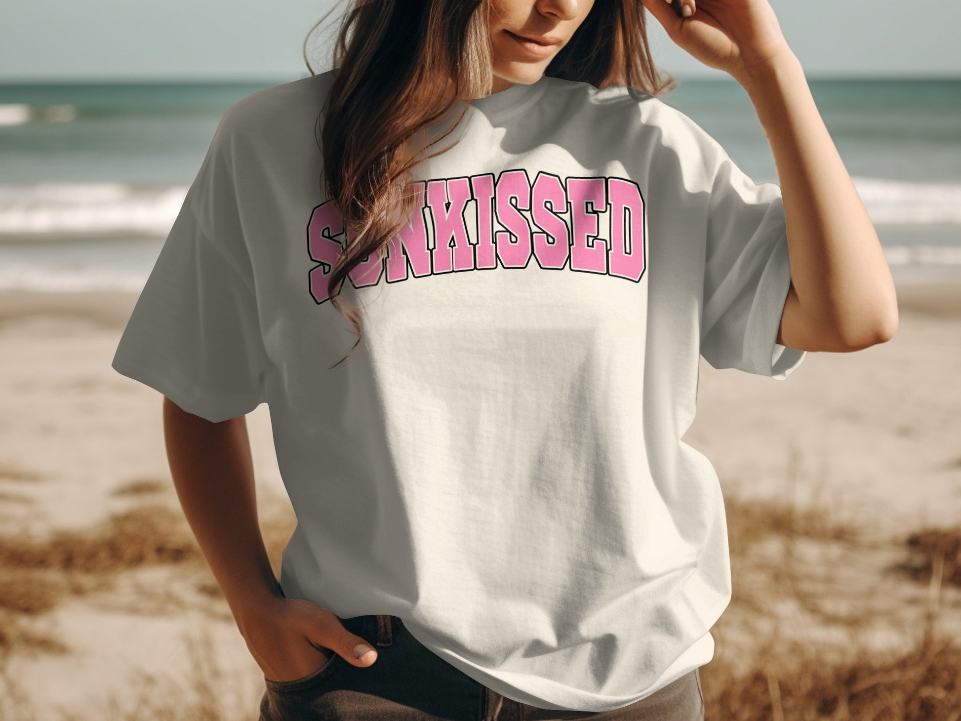White t-shirt with "SUN-KISSED" text on the chest, worn by a person on a beach.