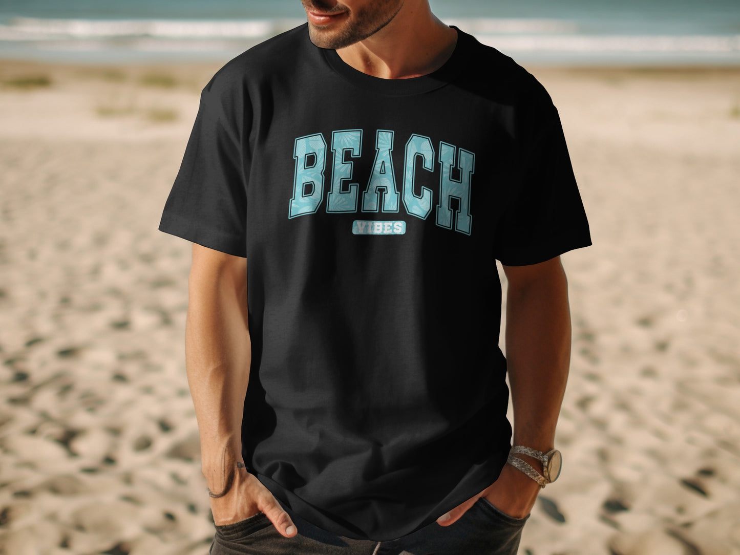Black t-shirt with "BEACH VIBES" text on a man standing on a beach.