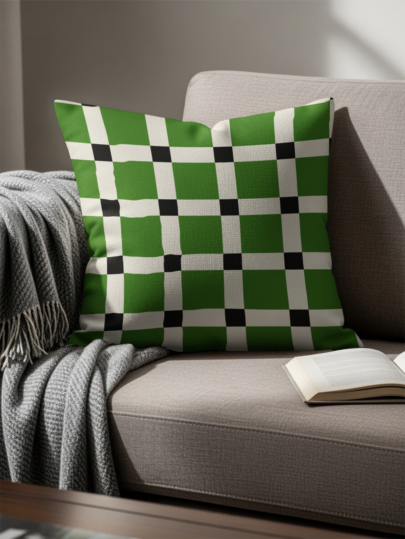 Green, white, and black checkered pillow on a grey couch with a blanket.