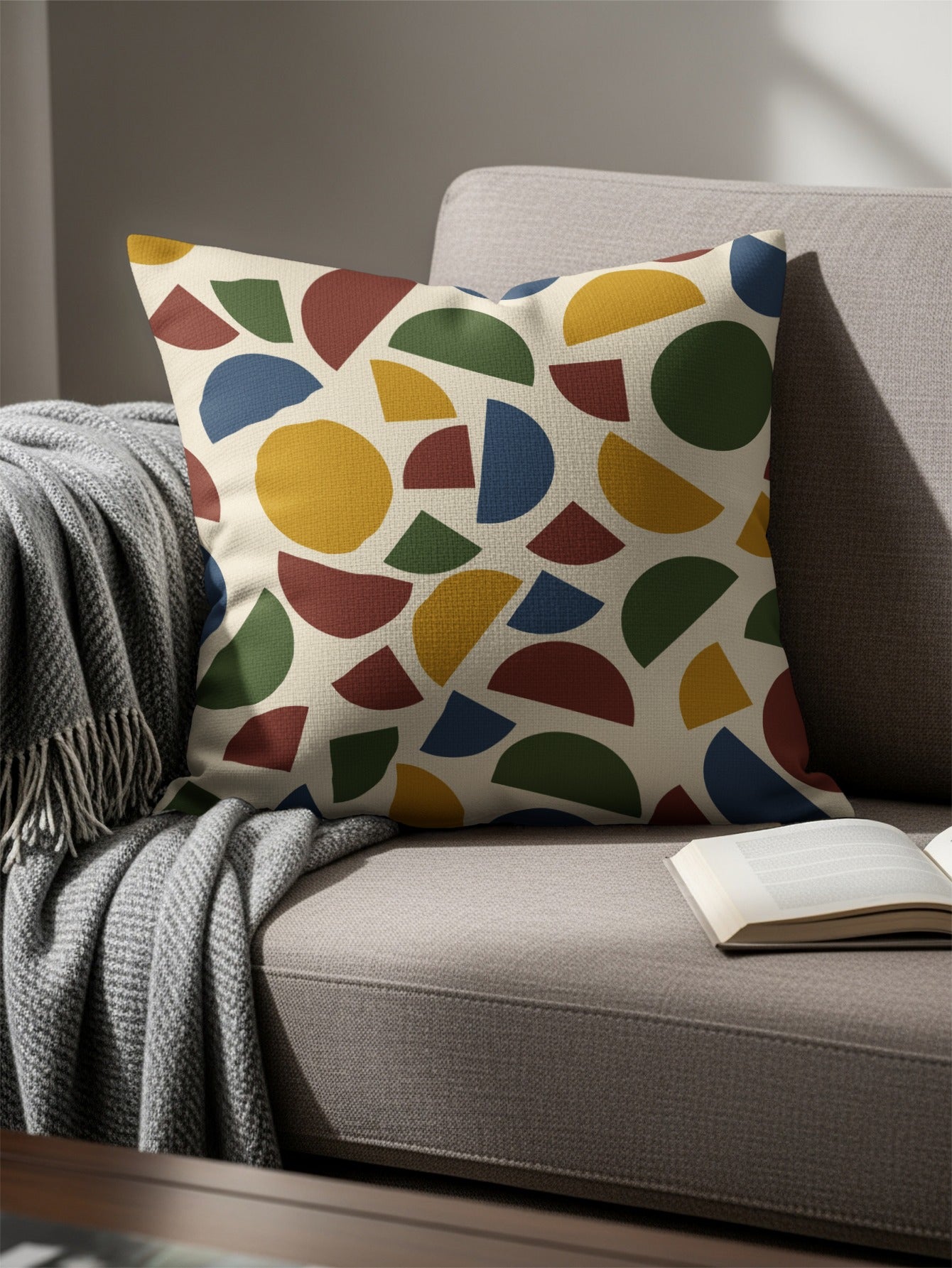 Decorative pillow with abstract geometric pattern on a couch with a blanket and book.